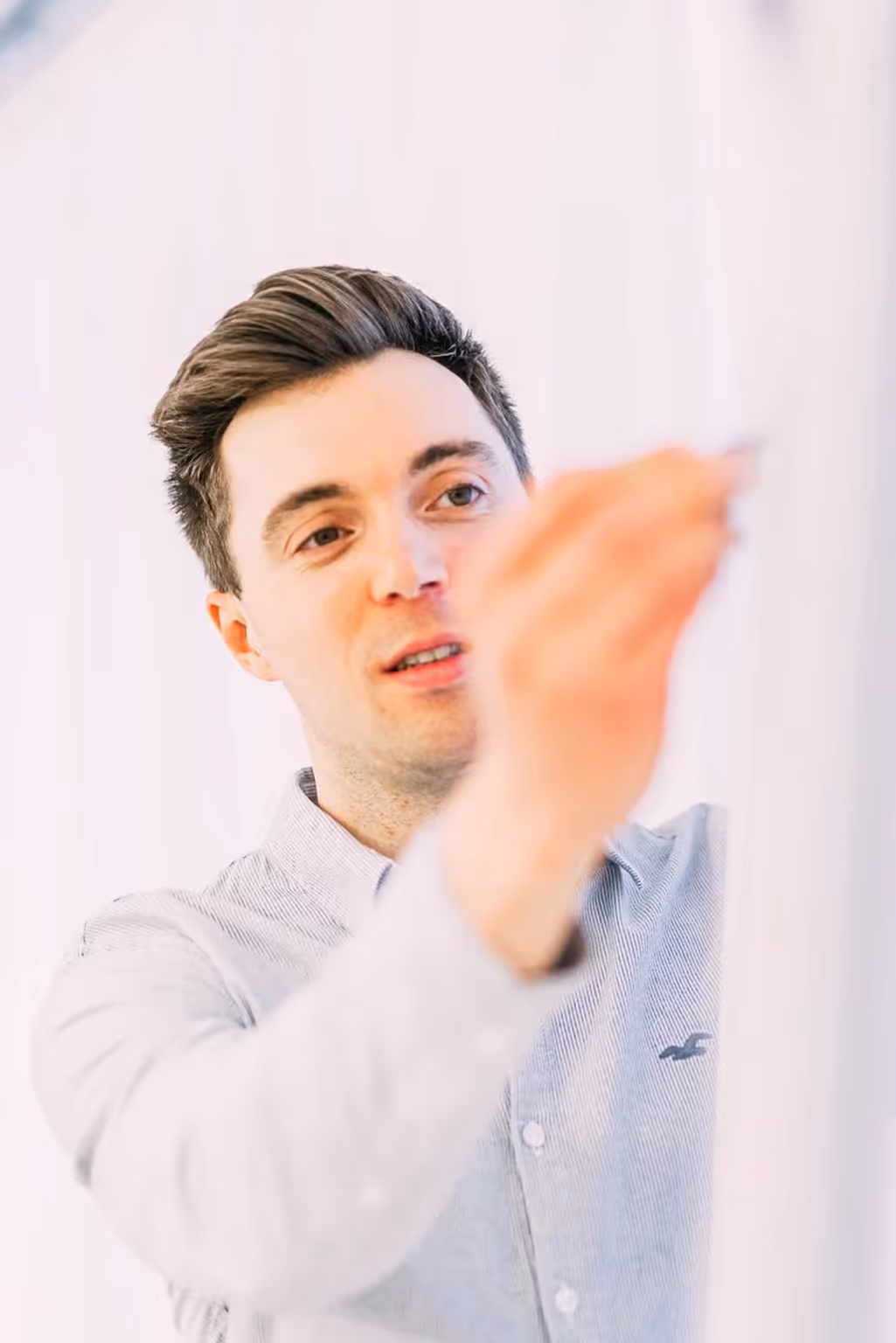 Man in a light blue button-up shirt writing on a transparent board.